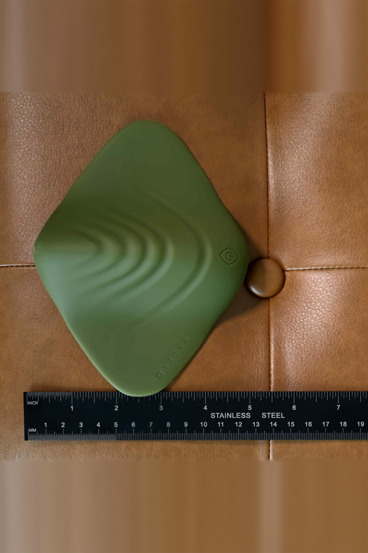 All the Pleasure grinding pad in Olive Green on brown leather next to a ruler, showing its width and diamond shape from above