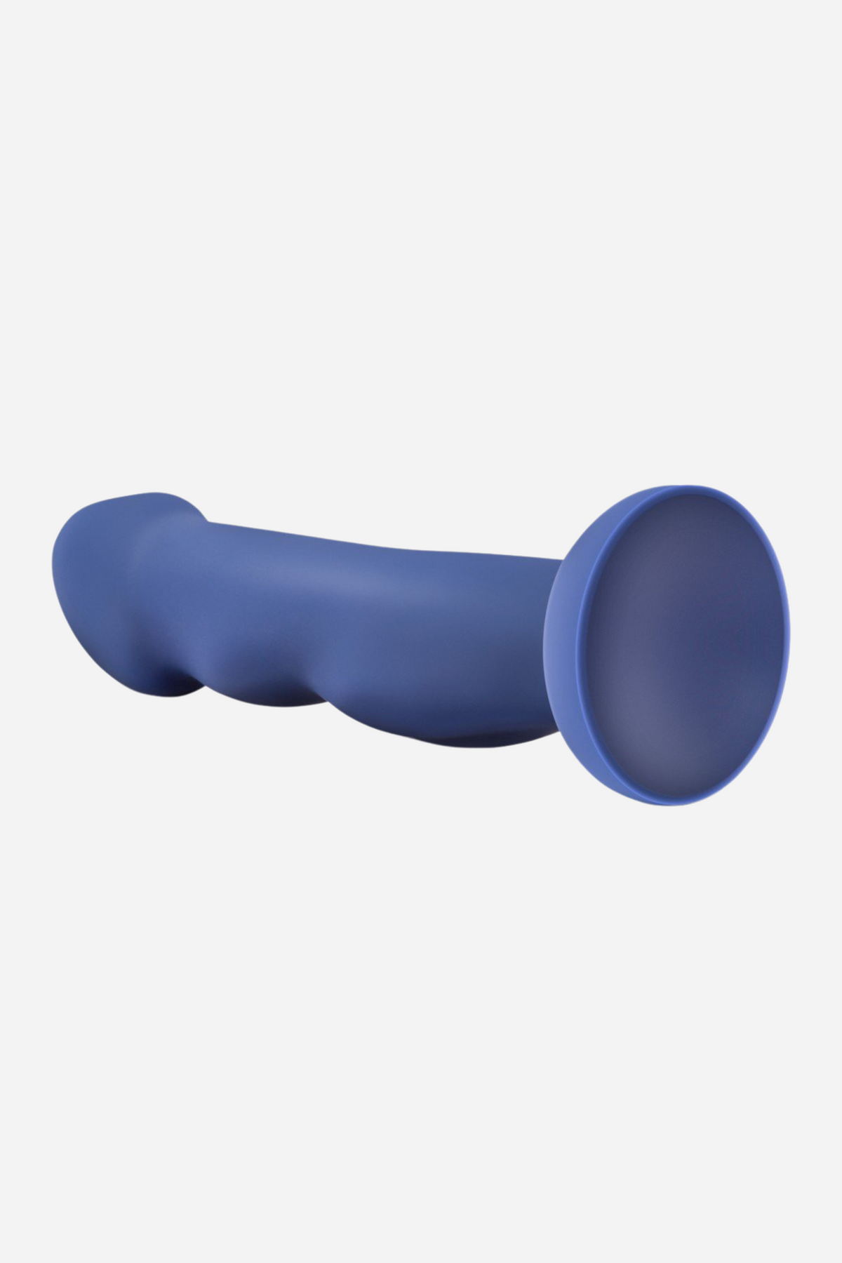 The indigo dildo lying on its side, angled so the flat round suction cup faces the camera and the sculpted underside is visible.