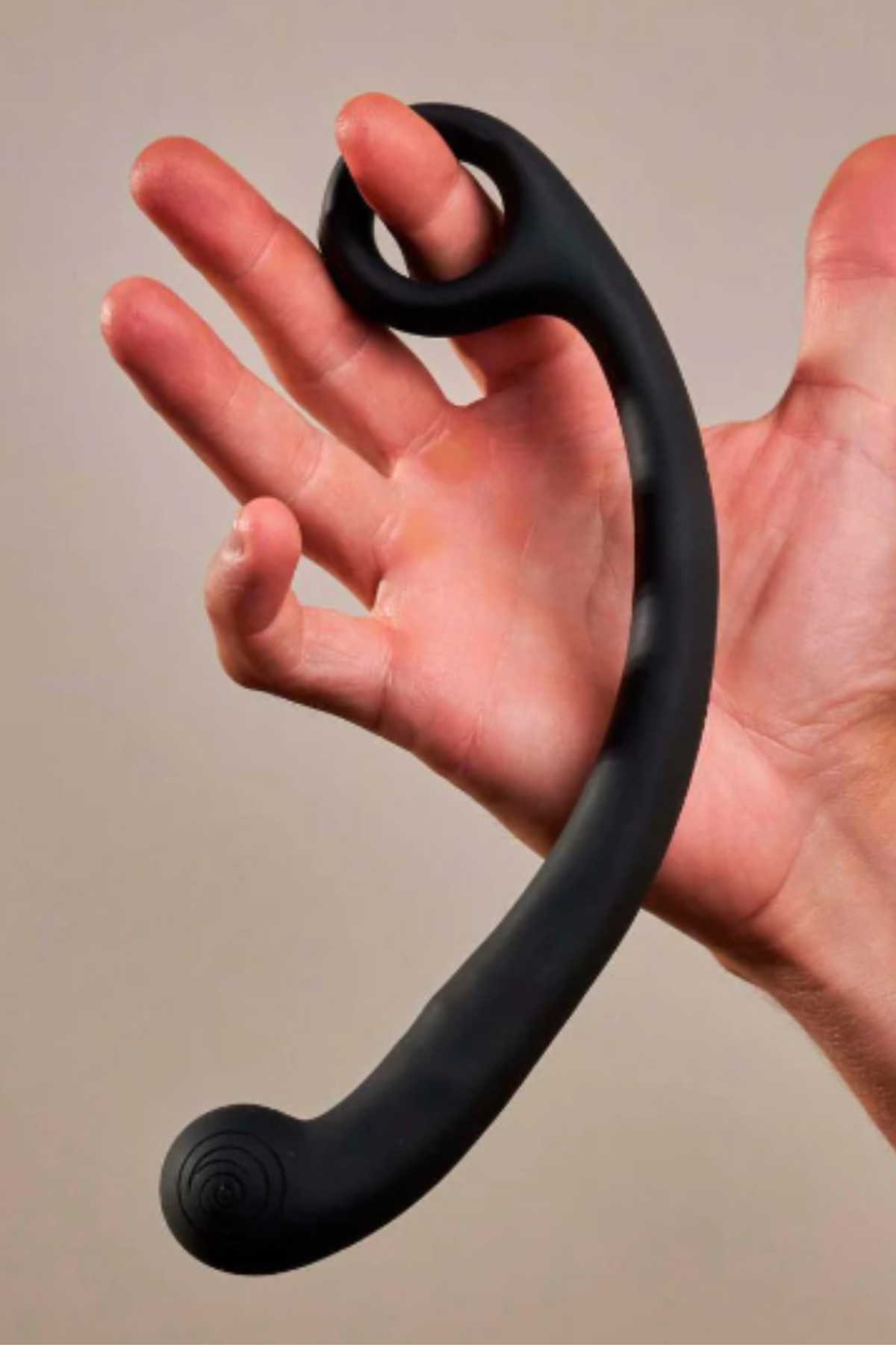 Hand holding the Axi Slimline G-spot wand in Granite Noir by its finger loop, showing the long curved shaft and rounded vibrating tip