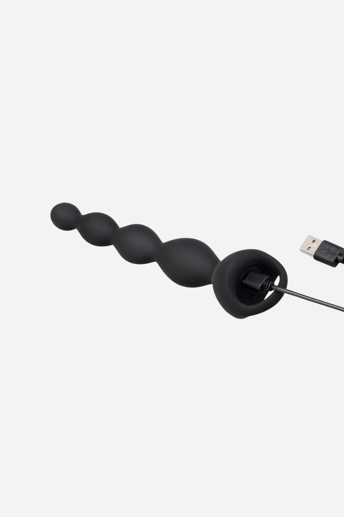 Black B-Vibe Earth Rumbling vibrating anal beads connected to the USB magnetic charging cable at the ring handle base, on grey