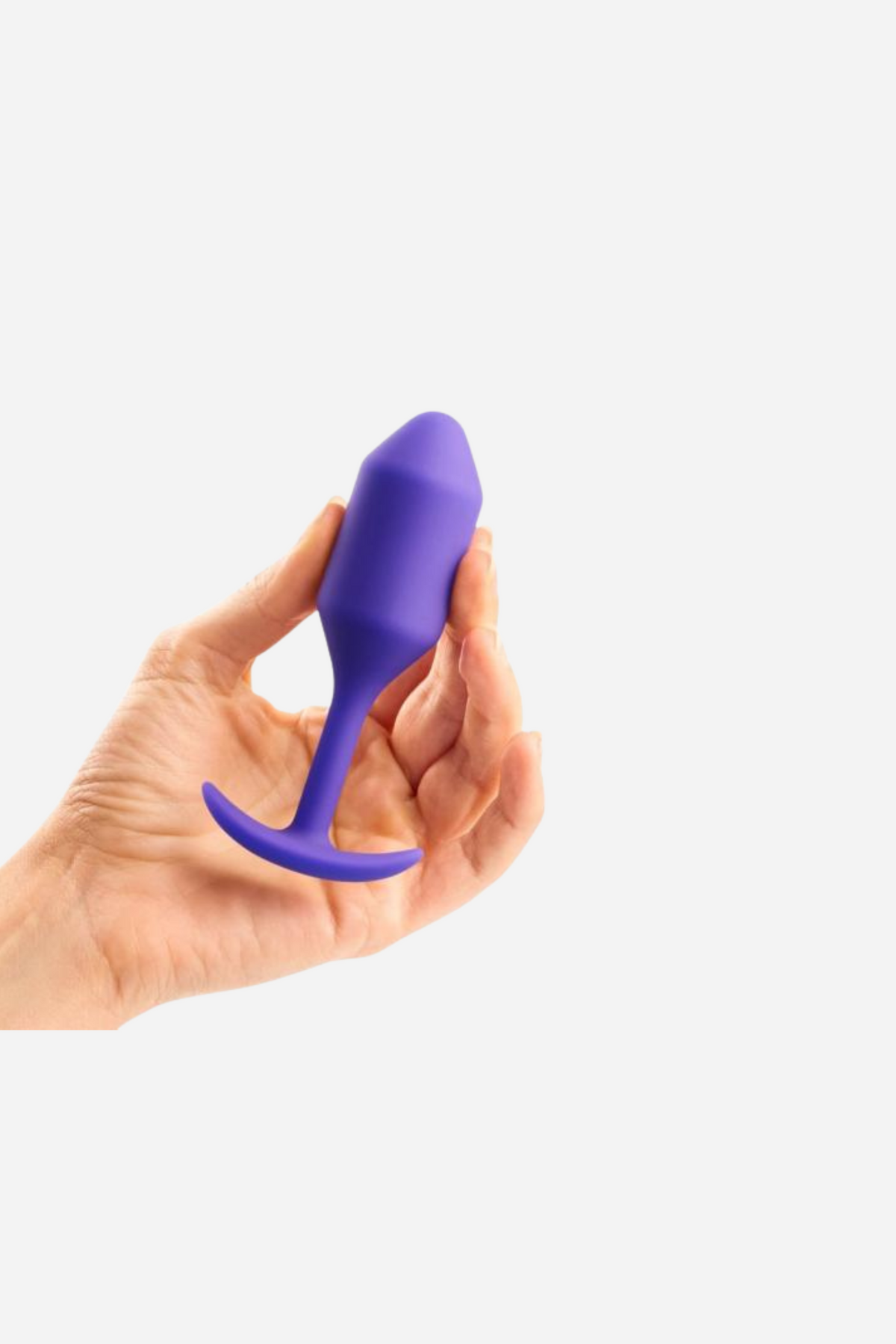 Hand holding the B-Vibe Snug Plug 2 in purple, a medium weighted silicone anal plug with a tapered tip, slim neck and flat T-shaped base