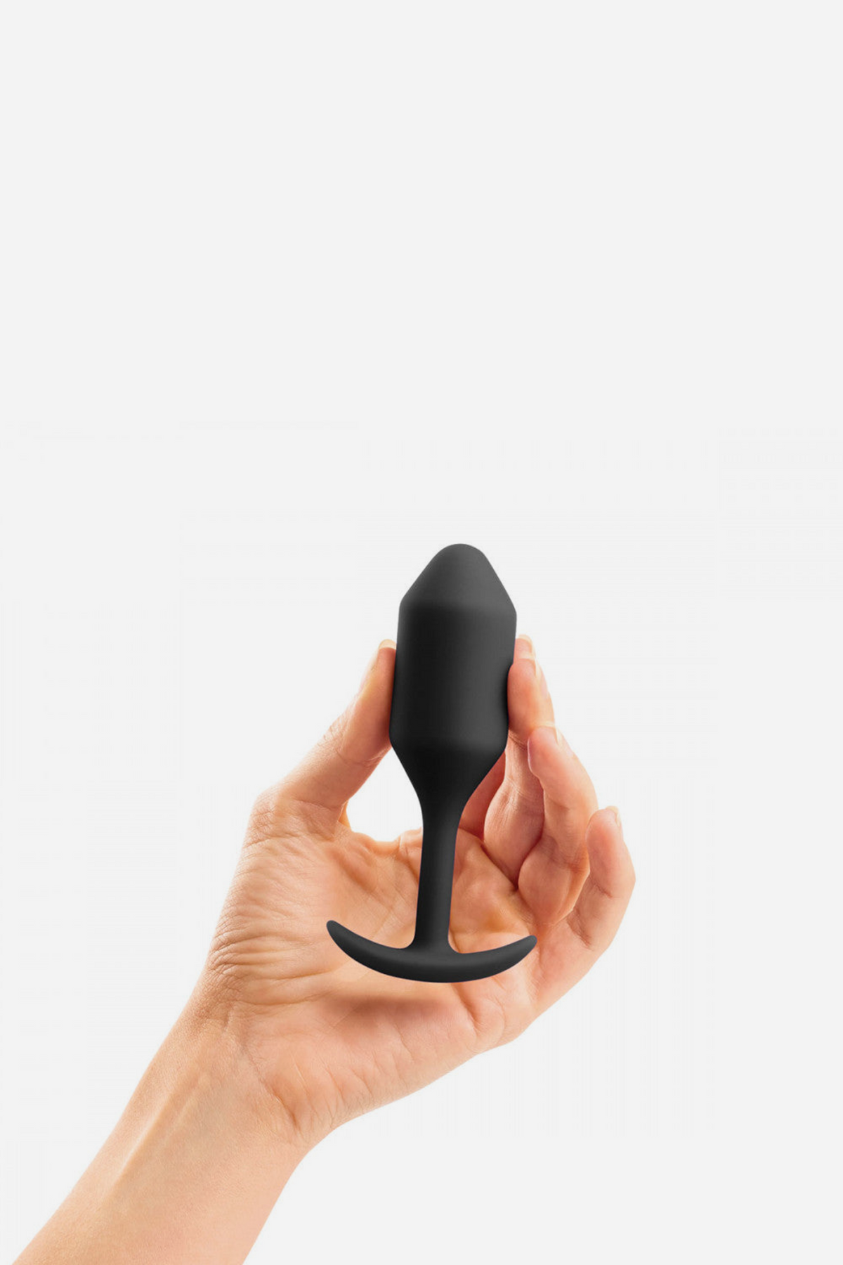 Hand holding the black B-Vibe Snug Plug 2 upright between the fingers, showing the size of this medium weighted anal plug for fullness