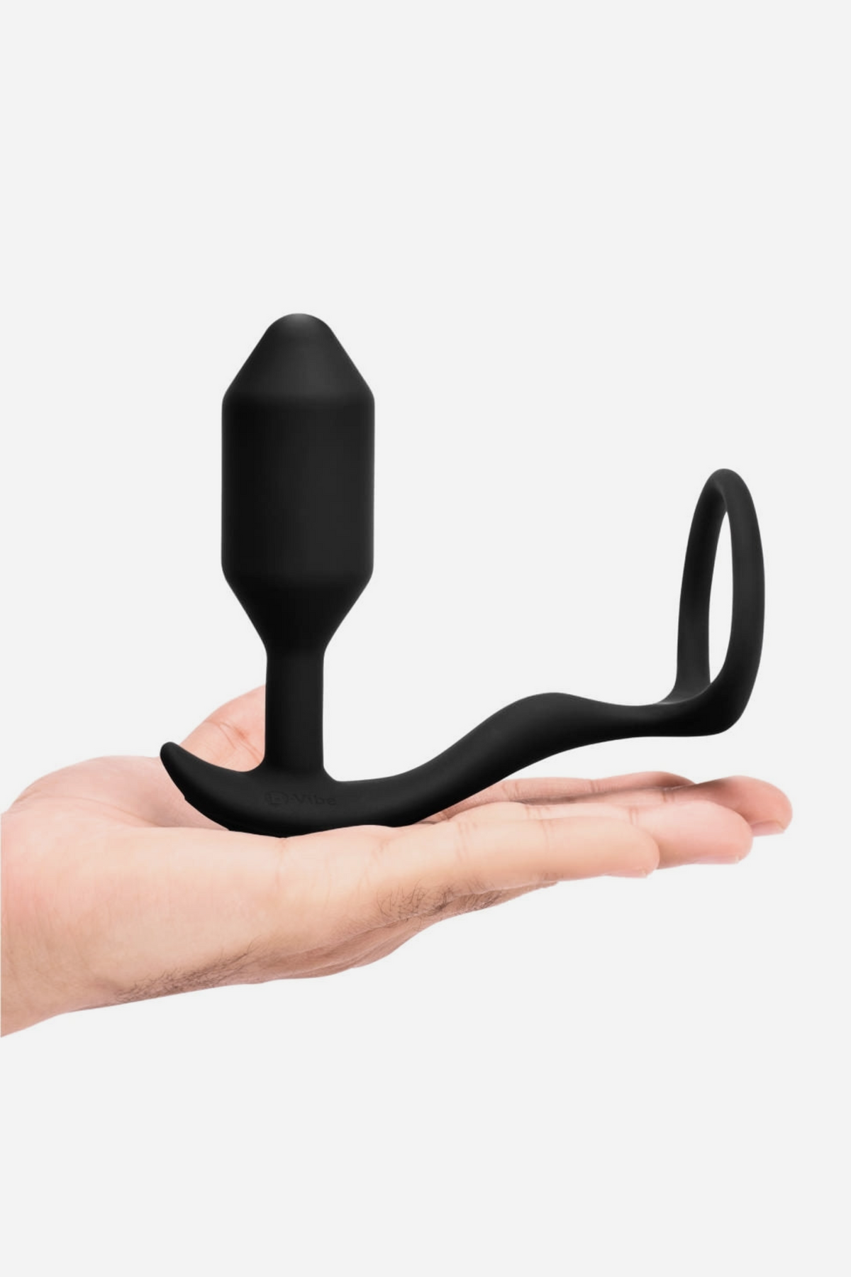 Hand holding the black B-Vibe Vibrating Snug and Tug cock ring plug flat on the palm to show its size and flexible ring, on grey