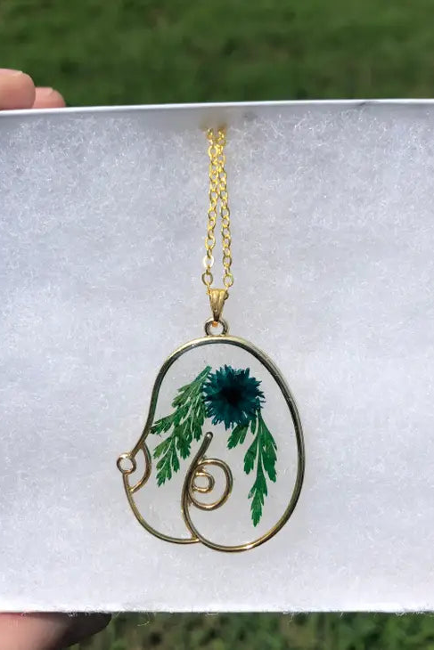 Gold wire Boob Floral Resin Necklace pendant shaped like a pair of breasts, filled with clear resin, a pressed blue flower and green fern
