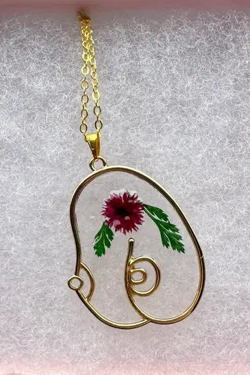 Boob Floral Resin Necklace in gold with a pressed magenta flower and green leaves set in clear resin, hanging on a fine gold chain