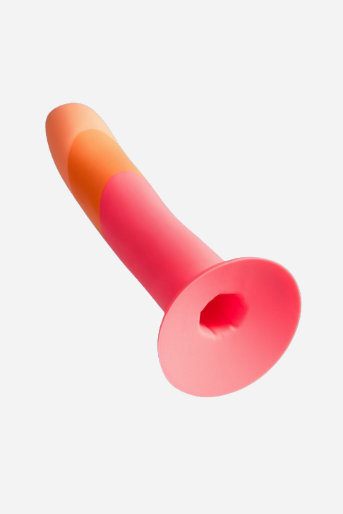 The dildo lying at an angle with its wide flared suction base facing the camera, the pink shaft and coral tip receding behind it.
