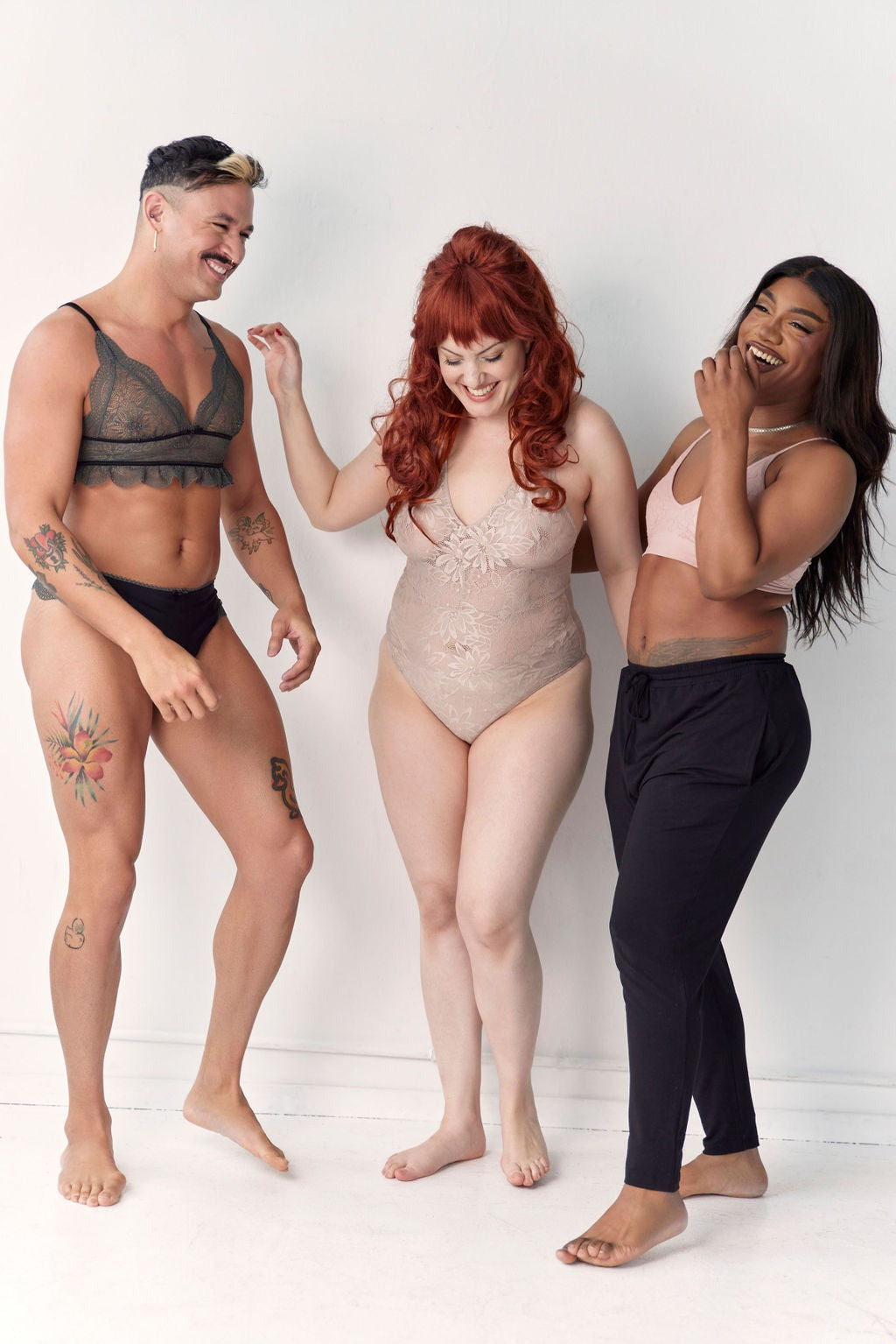 Three models standing together against a white wall, one wearing the Floruisse Ru lace bralette and thong set in slate sage