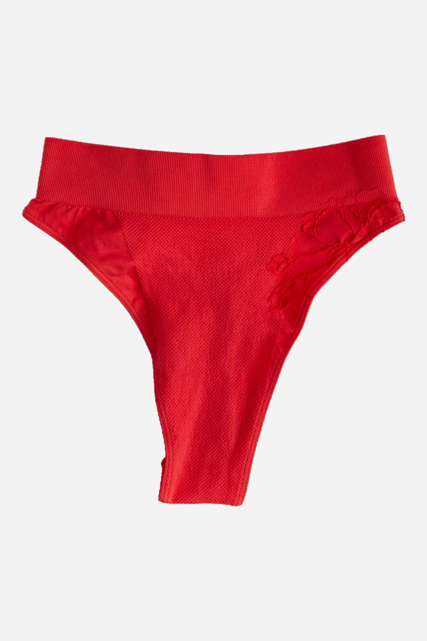 Flat lay of the Floruisse Dana seamless knit gaff in hot coral with a wide ribbed waistband and floral jacquard detail at the hip