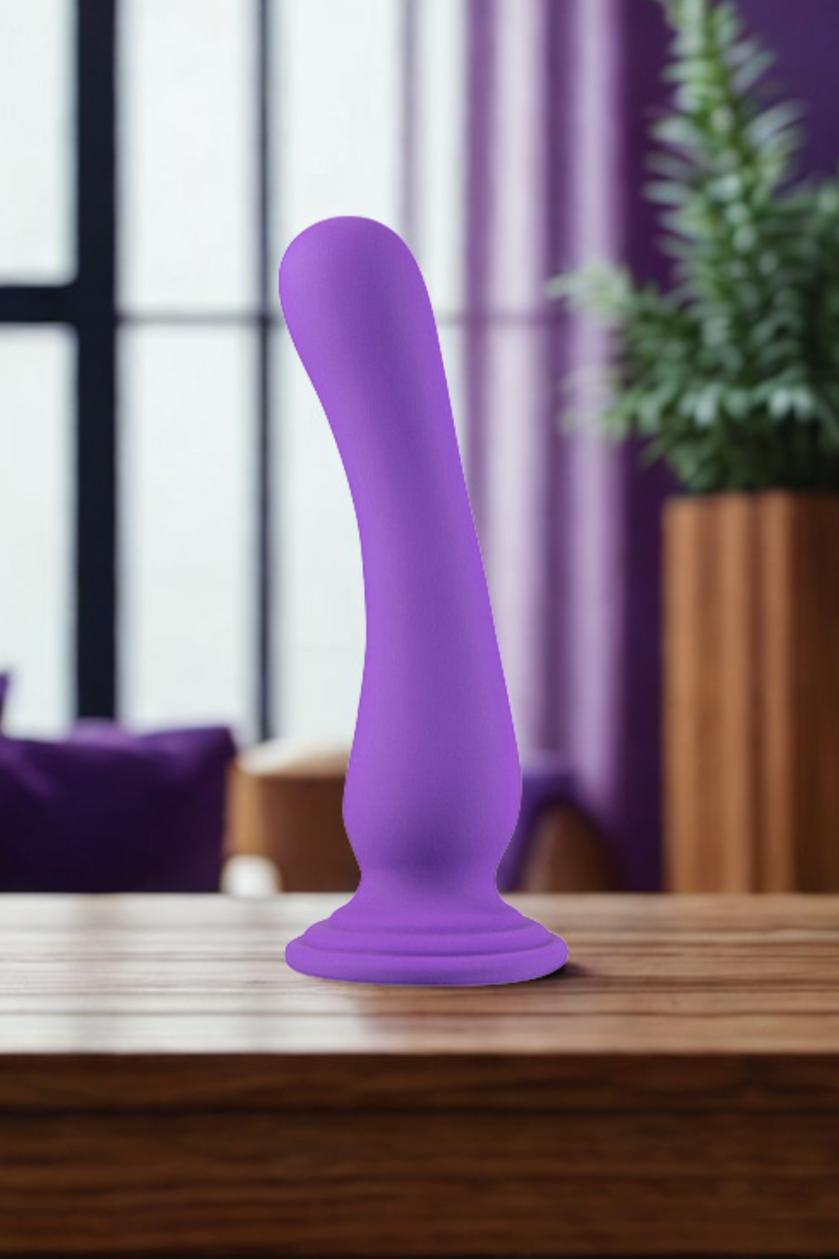 The purple dildo standing on a polished wooden table in a sunlit living room, with purple curtains, a window and a potted plant behind it.