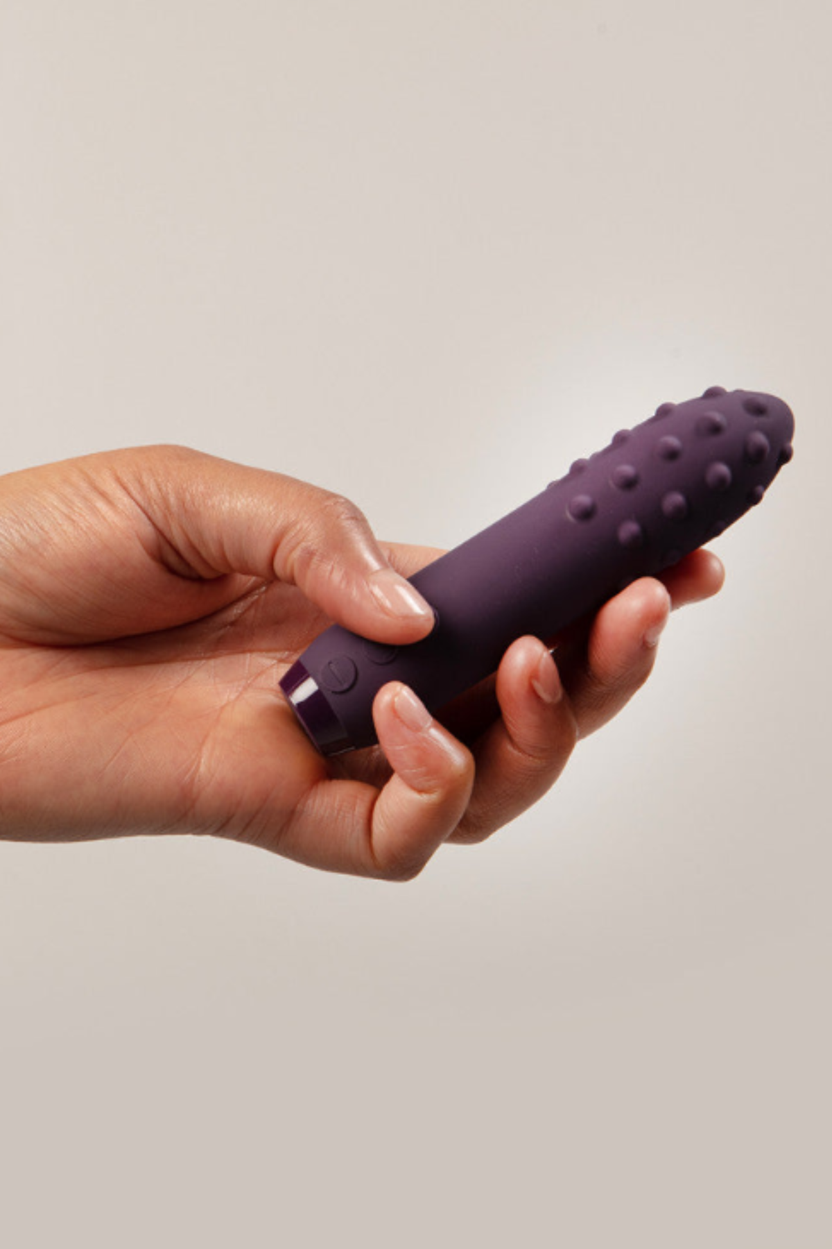 Je Joue Duet textured bullet vibrator in Purple held between two hands, showing its compact size and textured tip, on a soft grey wall