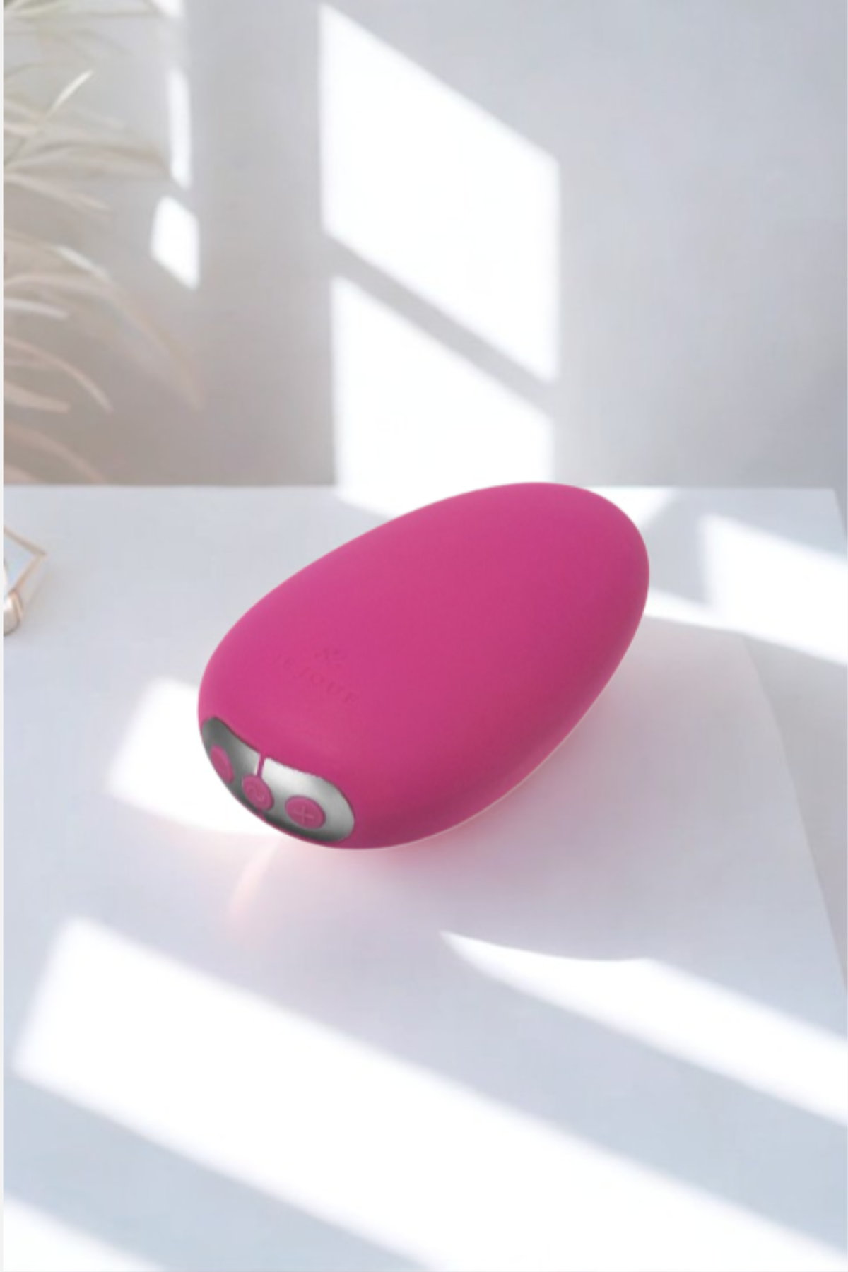 Fuchsia Je Joue Mimi Soft palm vibe resting on a white table in bright window sunlight, soft shadows falling across its rounded pebble shape.
