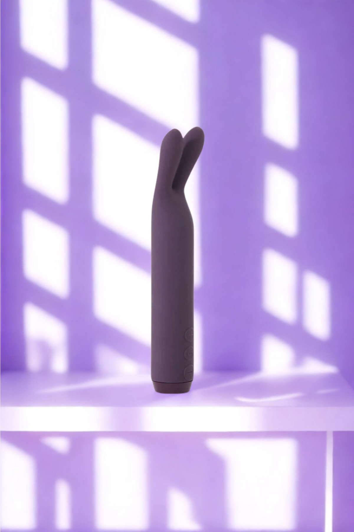 Purple Je Joue Rabbit Bullet Vibrator standing on a lilac shelf in dappled window light, a lifestyle shot of the compact bunny-eared bullet