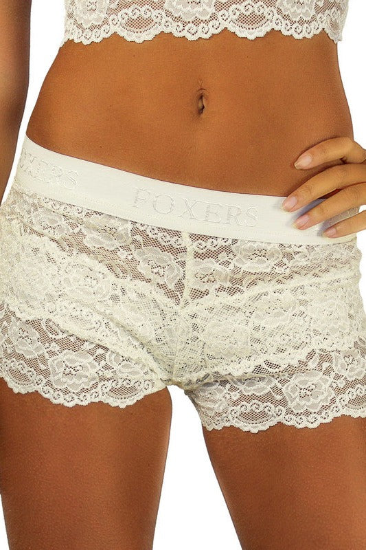 Front view of a model with a hand on her hip in ivory Foxers lace boxers with an ivory FOXERS waistband and a matching ivory lace top