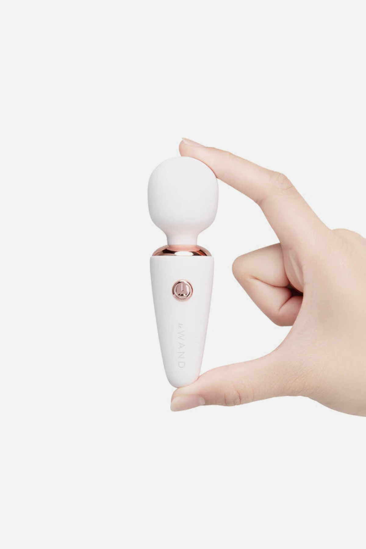 Le Wand Mini Micro Wand in white with rose gold trim, held between finger and thumb to show its compact pocket-friendly size