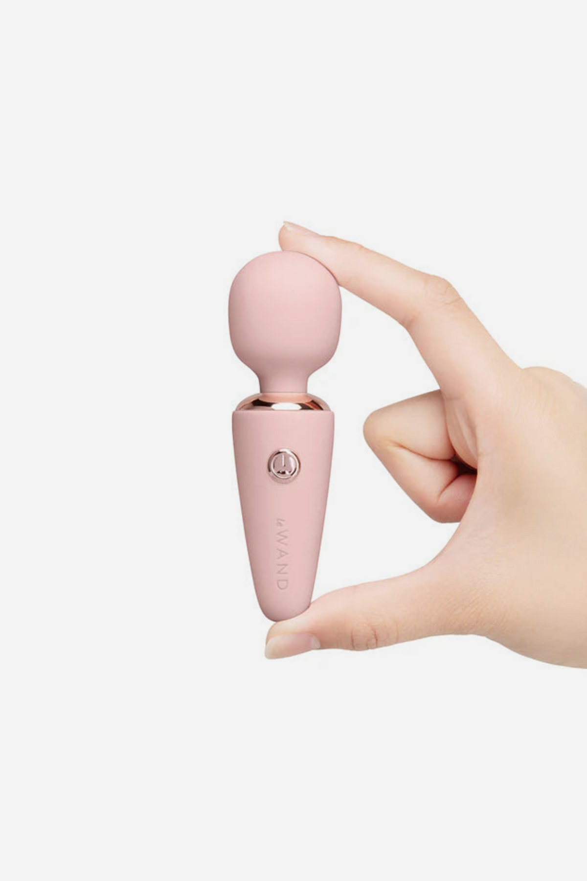 Le Wand Mini Micro Wand in light pink with rose gold trim, held between finger and thumb to show its small travel-friendly size