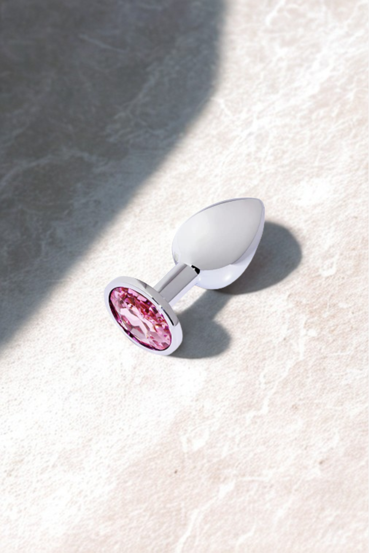 Silver Pretty Princess Butt Plug with a light pink gem resting on pale stone in soft sunlight, a lifestyle shot of the sparkling base