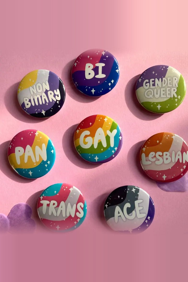 Eight hand-drawn pride flag identity buttons on pink: Nonbinary, Bi, Genderqueer, Pan, Gay, Lesbian, Trans and Ace