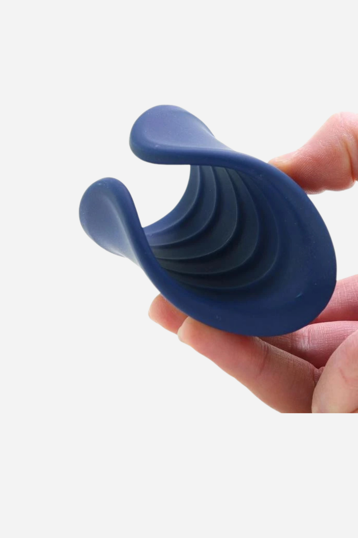 A hand holds the navy blue stroker, a curved manta-ray shape with layered ridges along its underside, against a plain grey backdrop.