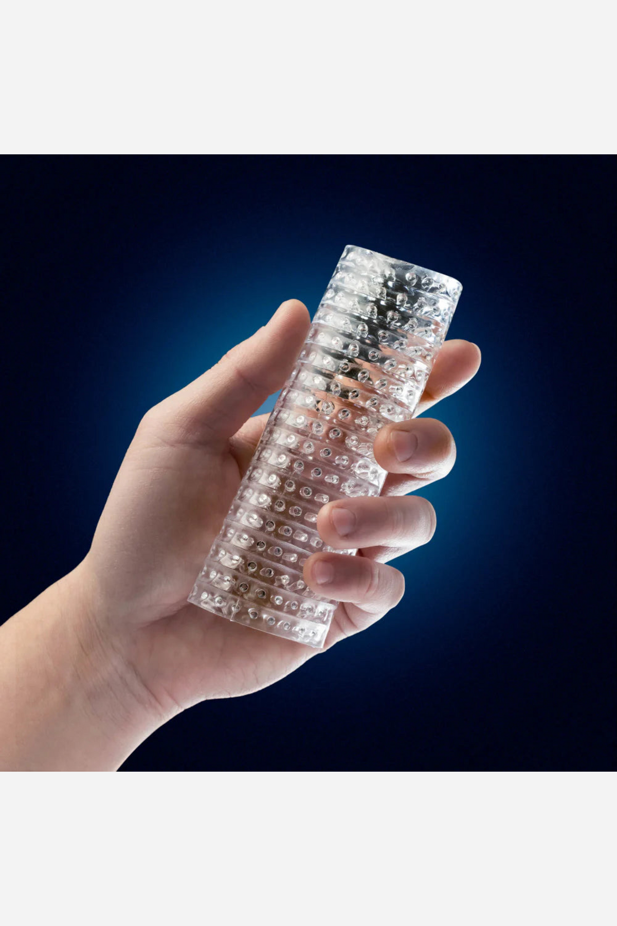 A hand holding the clear Strokez sleeve against a deep navy background, its raised diamond lattice textured across the clear barrel.