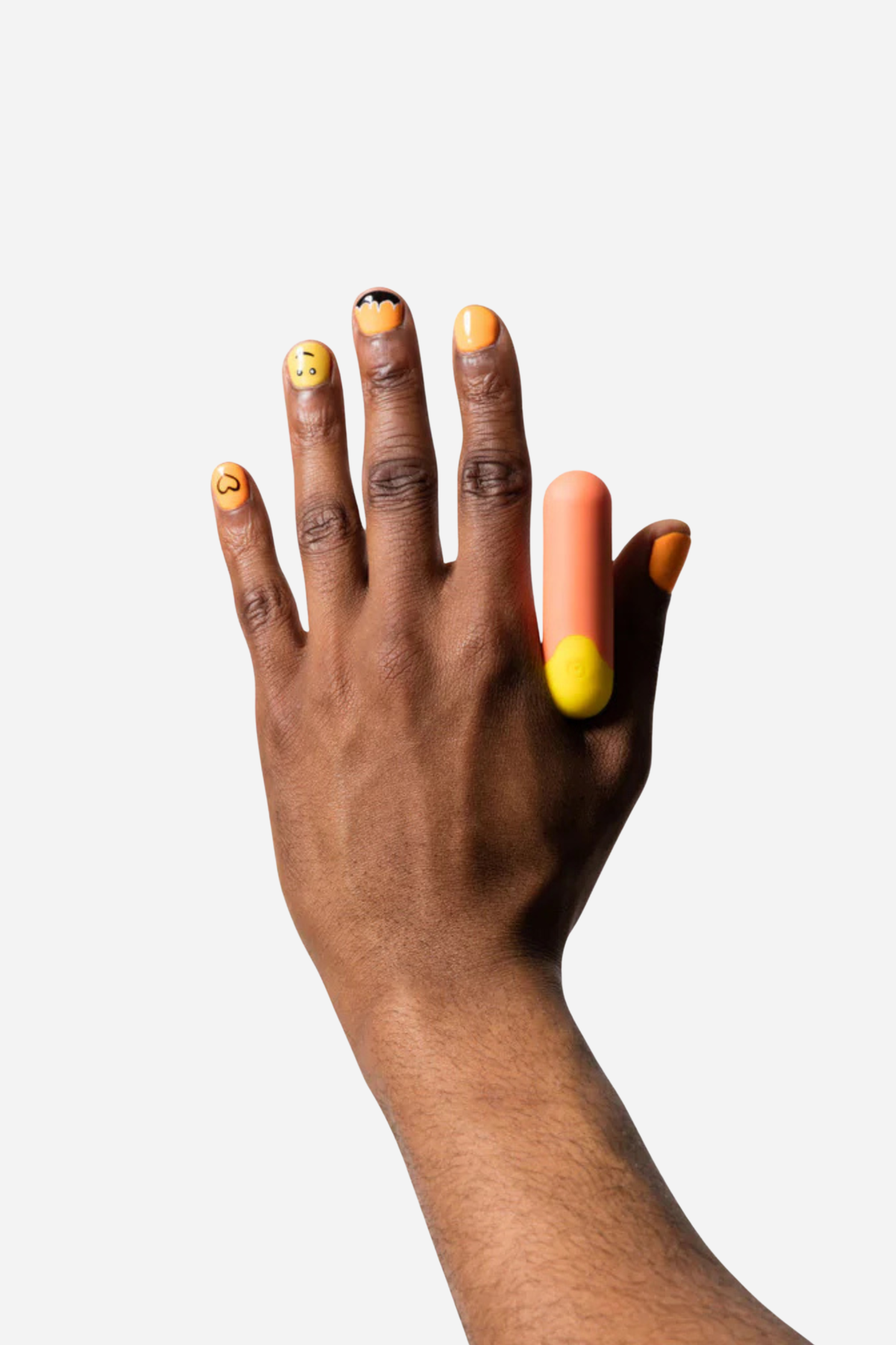 Romp Riot rechargeable bullet vibrator in coral and yellow worn between the fingers of a raised hand, shown on a light grey background