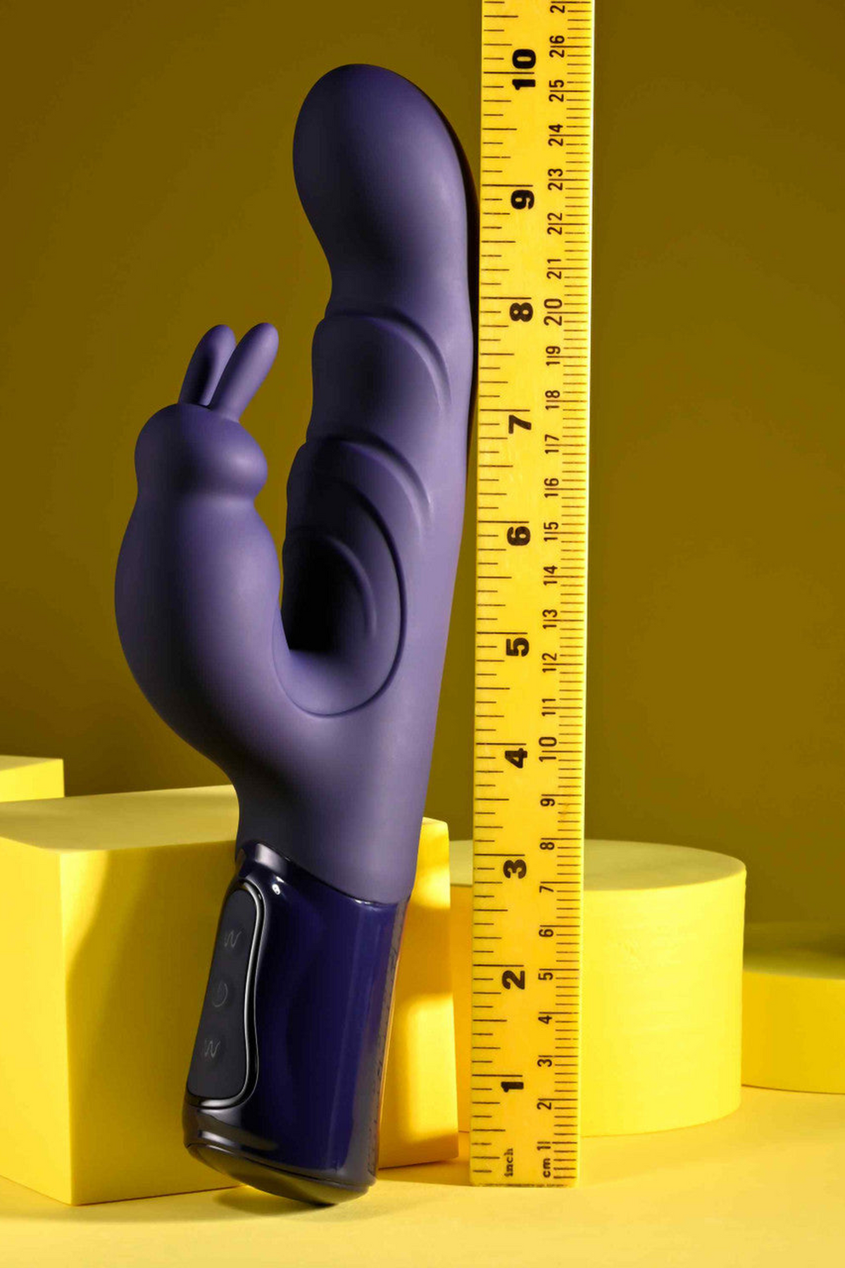 She's A Big Deal Rabbit Vibe standing upright on yellow blocks beside a tape measure, showing the length and girth of the purple rabbit vibrator