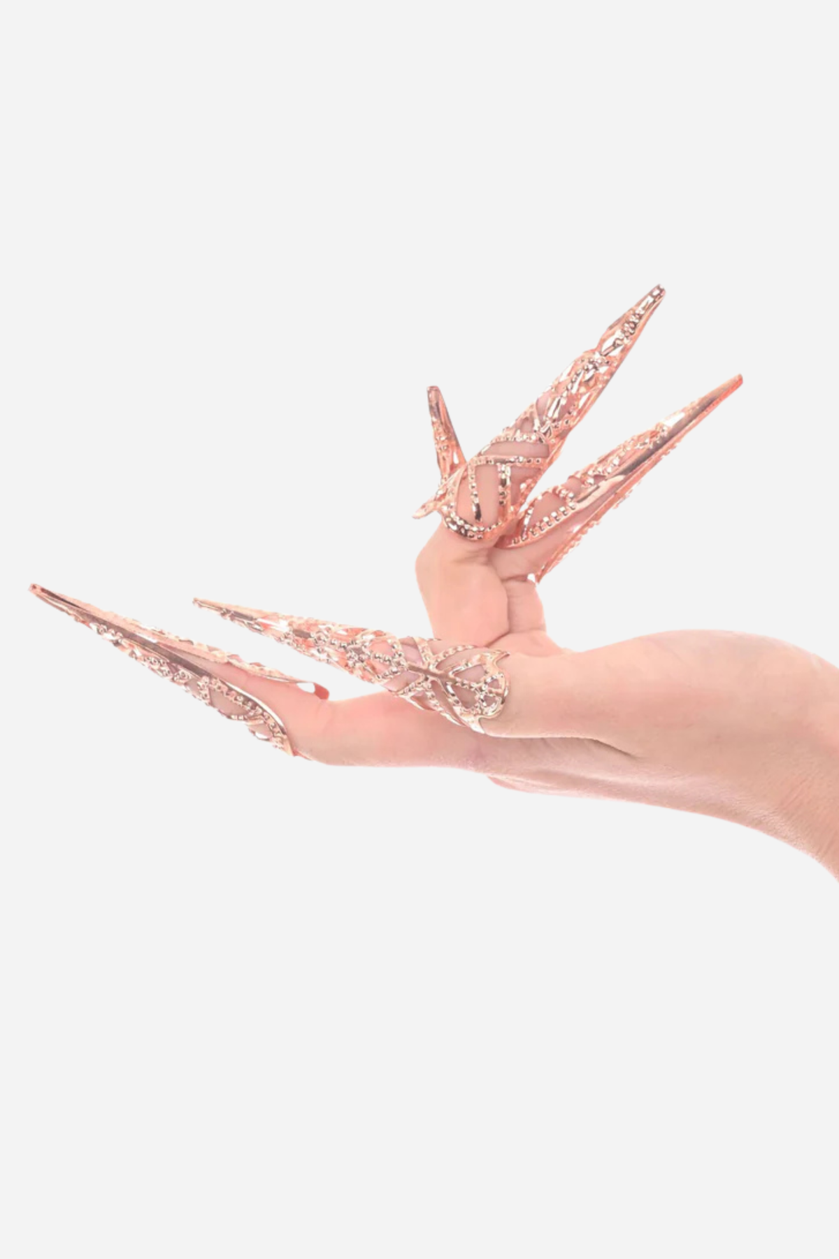 Hand wearing five She's A Brat rose gold sensation finger tips, long pointed filigree claws fanned out over a light grey background