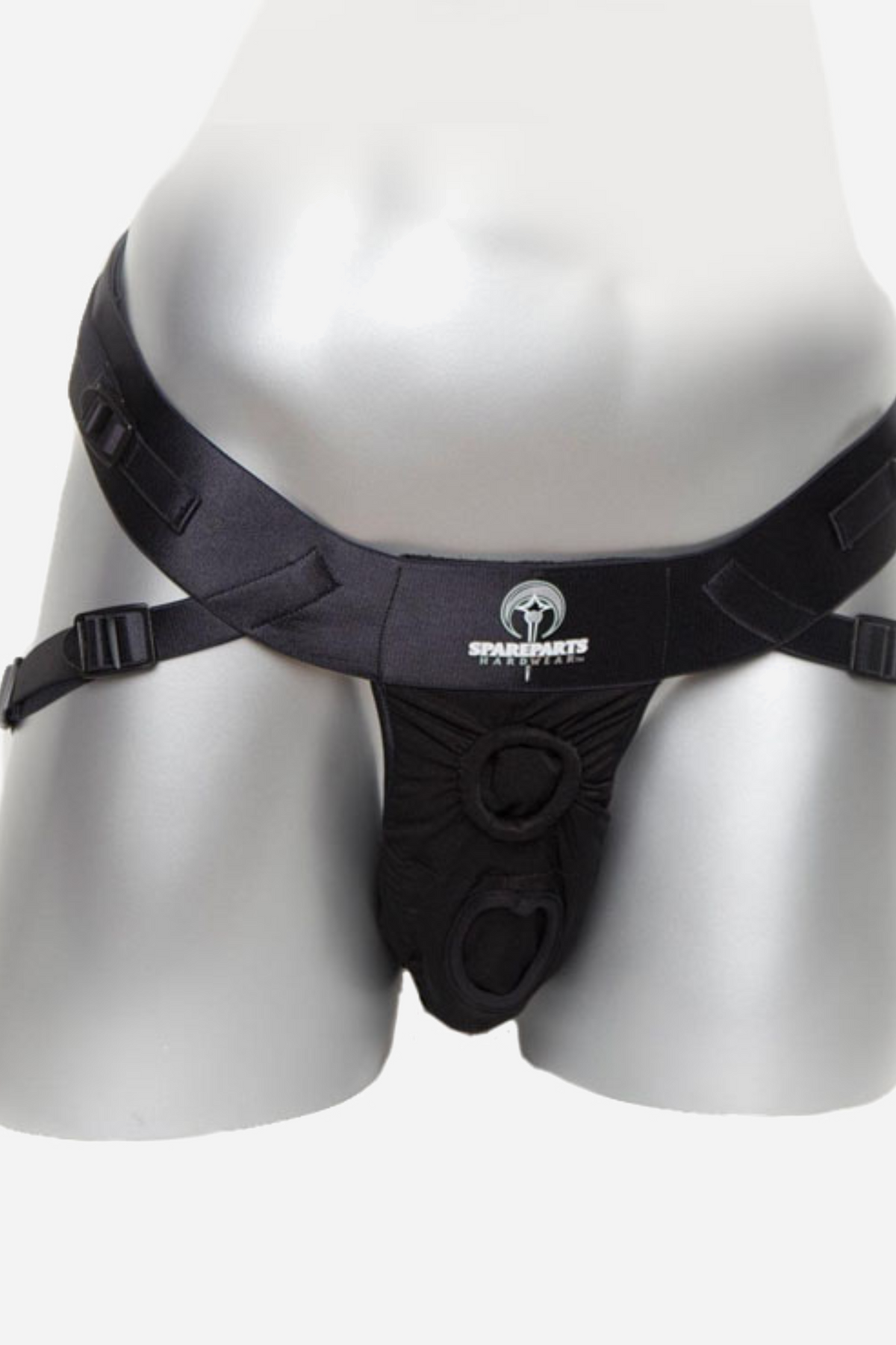 A black fabric strap-on harness fitted on a pale grey mannequin, shown from the front with its wide waistband and O-ring opening.
