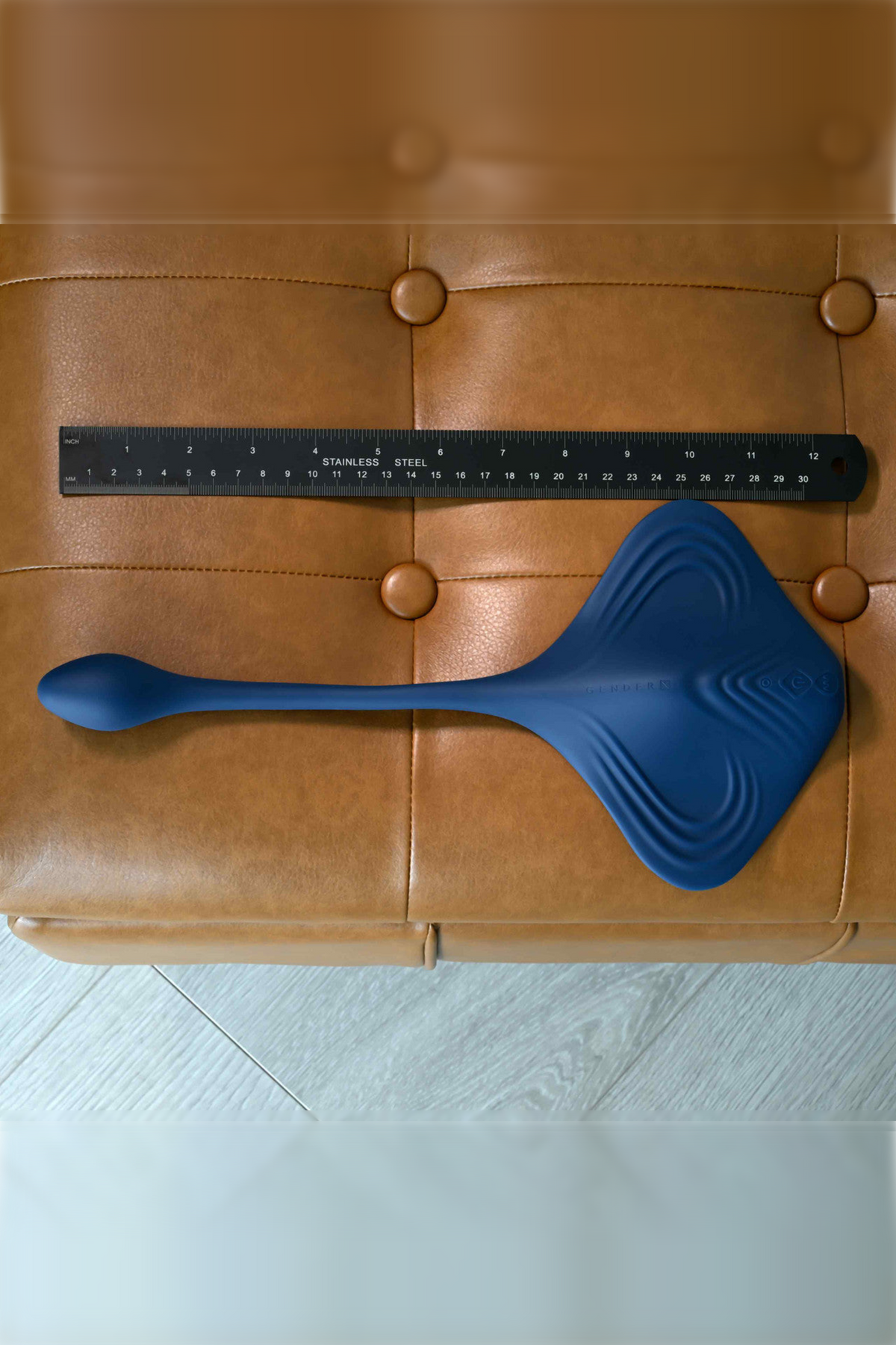 The Daily Grind pad laid on a tan leather ottoman beside a ruler, showing its size from the plug tip to the edge of the ridged pad