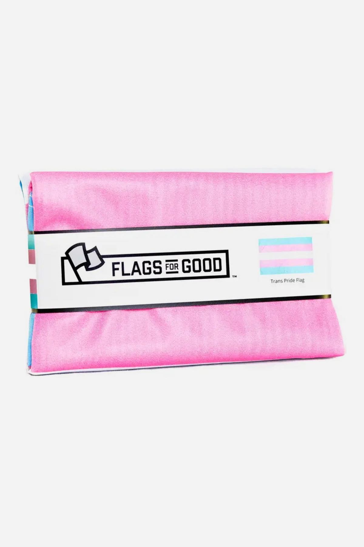 Trans pride flag folded in its packaging, wrapped with a white Flags for Good paper band showing the logo and a small blue, pink and white flag graphic.