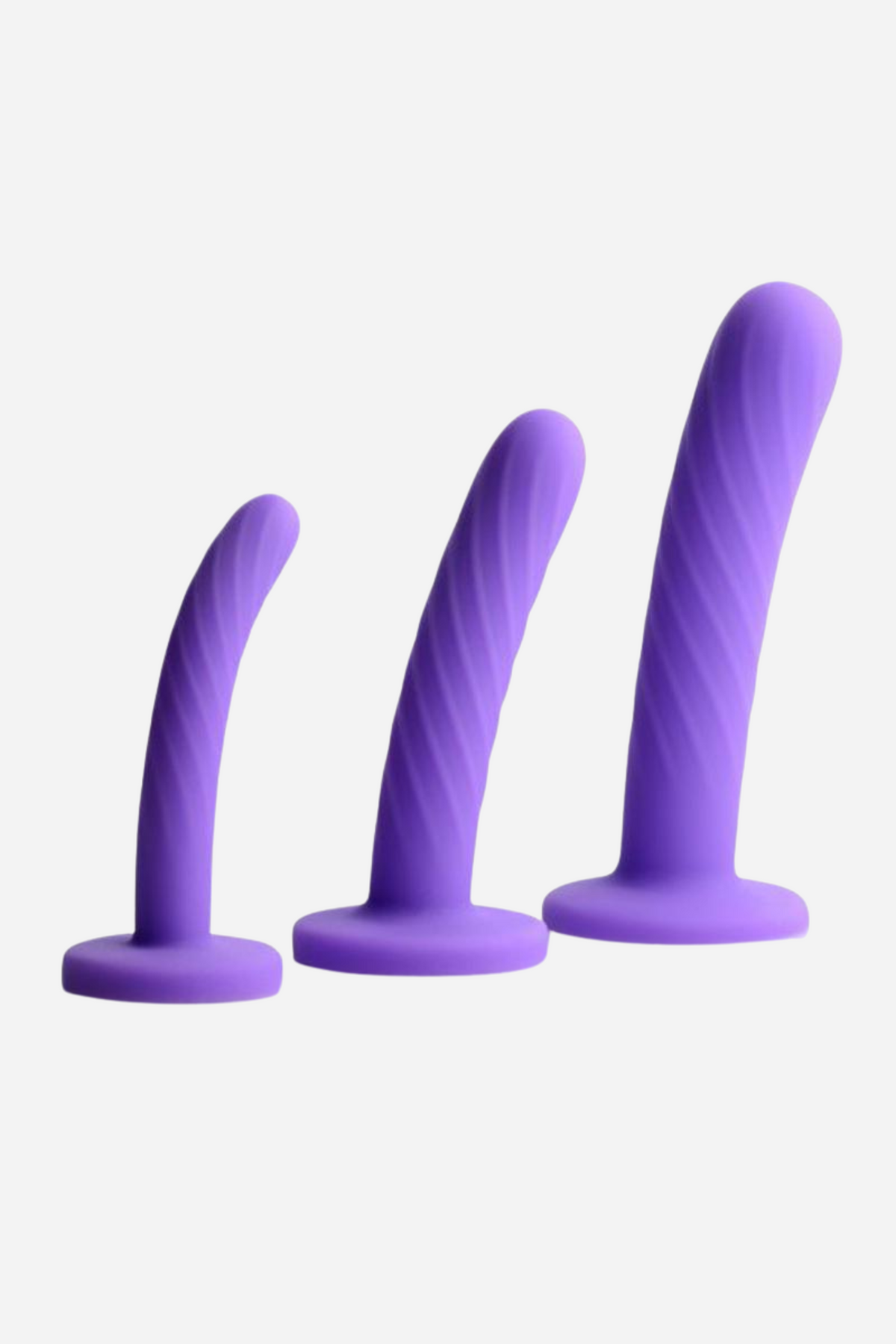 Three purple silicone dildos standing in a row on flared bases, graduating from small and smooth to tall with a spiralled shaft, on a grey backdrop.