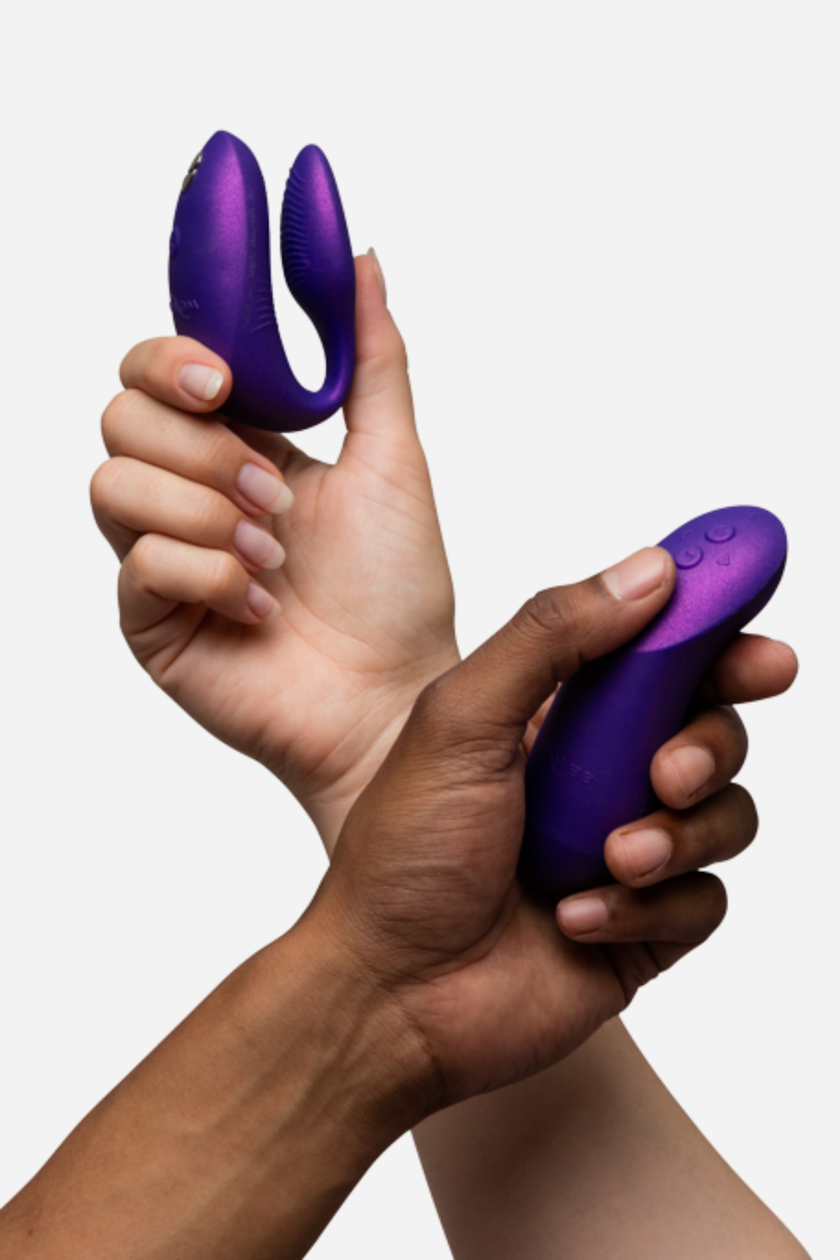 Two hands holding the We-Vibe Chorus Pro in Cosmic Purple, one with the couples vibrator and one squeezing the remote control