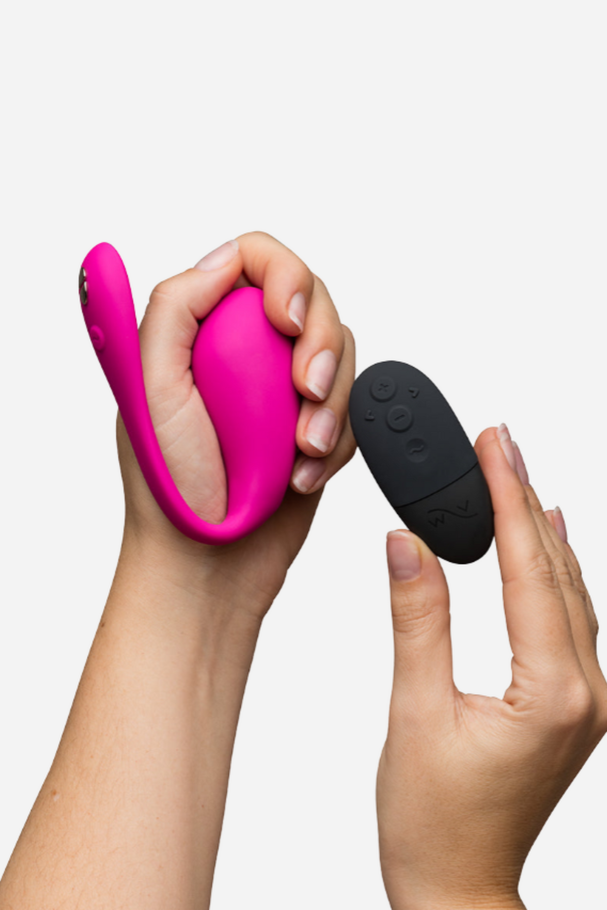 Hands holding the electric pink We-Vibe Jive 2 and its black pebble remote, showing how the wearable can be controlled discreetly