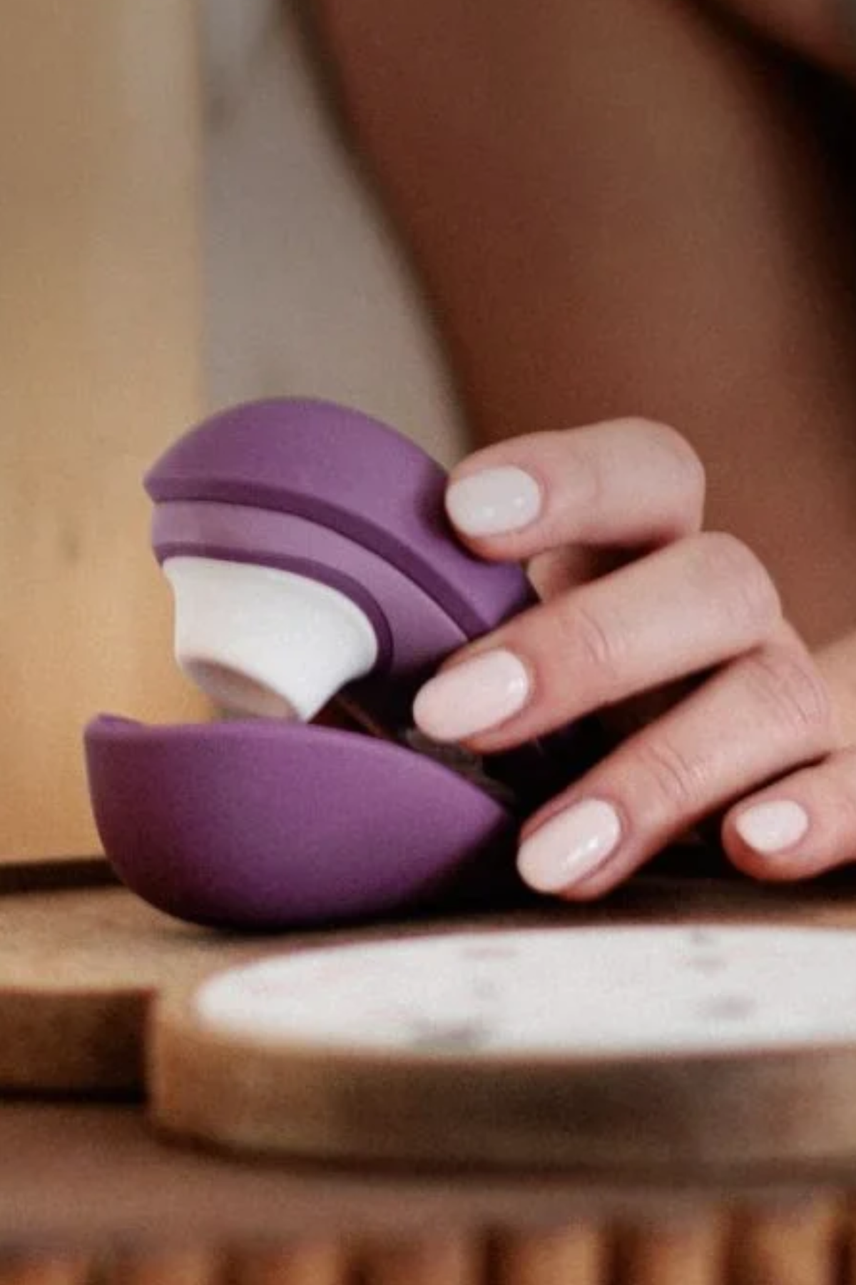 Hand opening the purple Womanizer Liberty 2 on a wooden tray, showing the magnetic travel lid that protects the soft silicone stimulation head