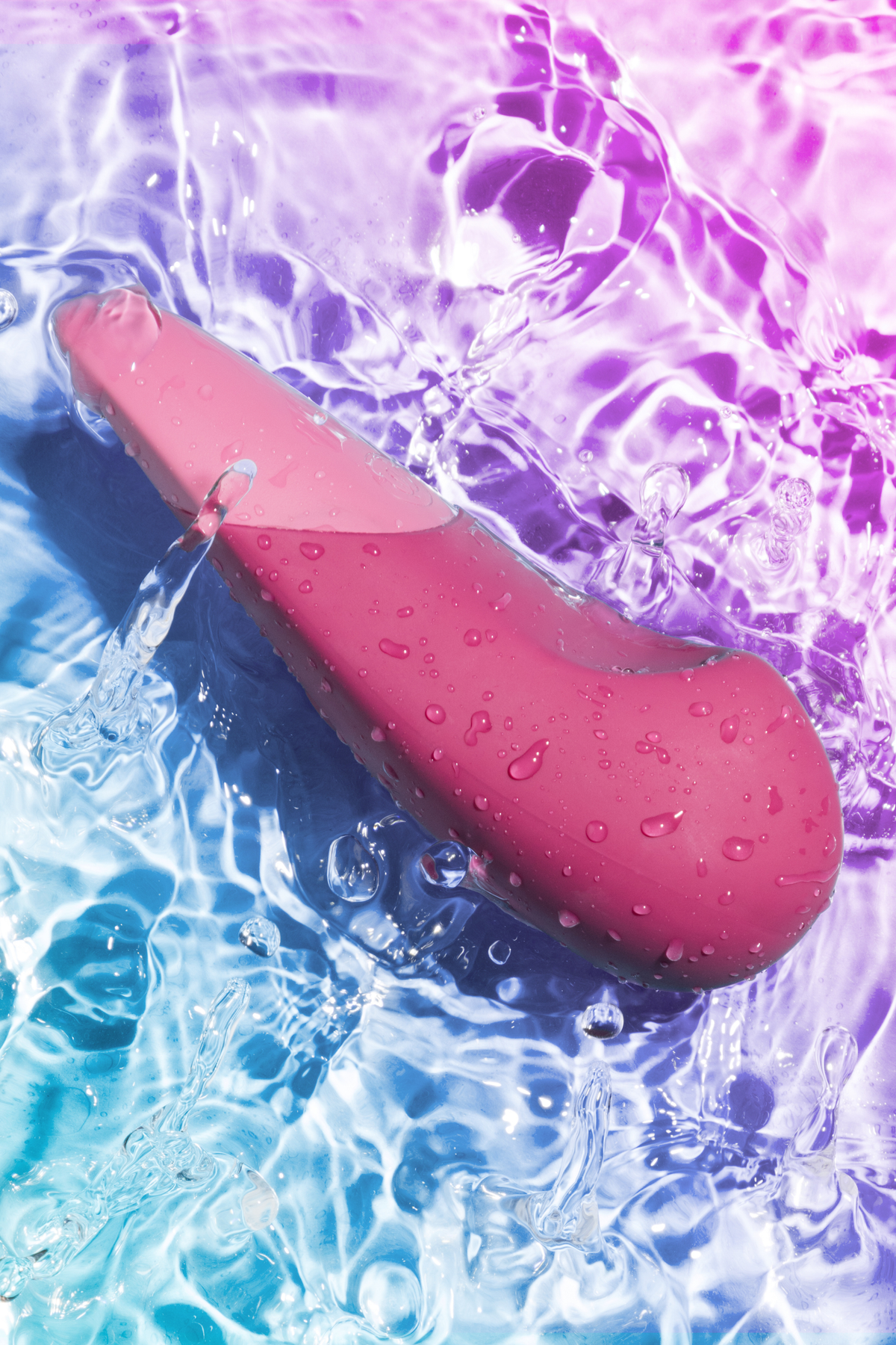 Dusty pink Womanizer Vibe lying in rippling water lit with blue and purple light, highlighting the fully waterproof body-safe silicone design