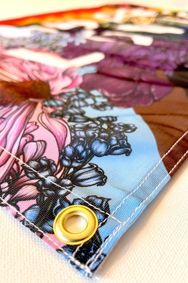 Close-up of a corner of the You Are Loved pride flag showing the brass grommet, stitched hem and colourful hand-drawn floral print