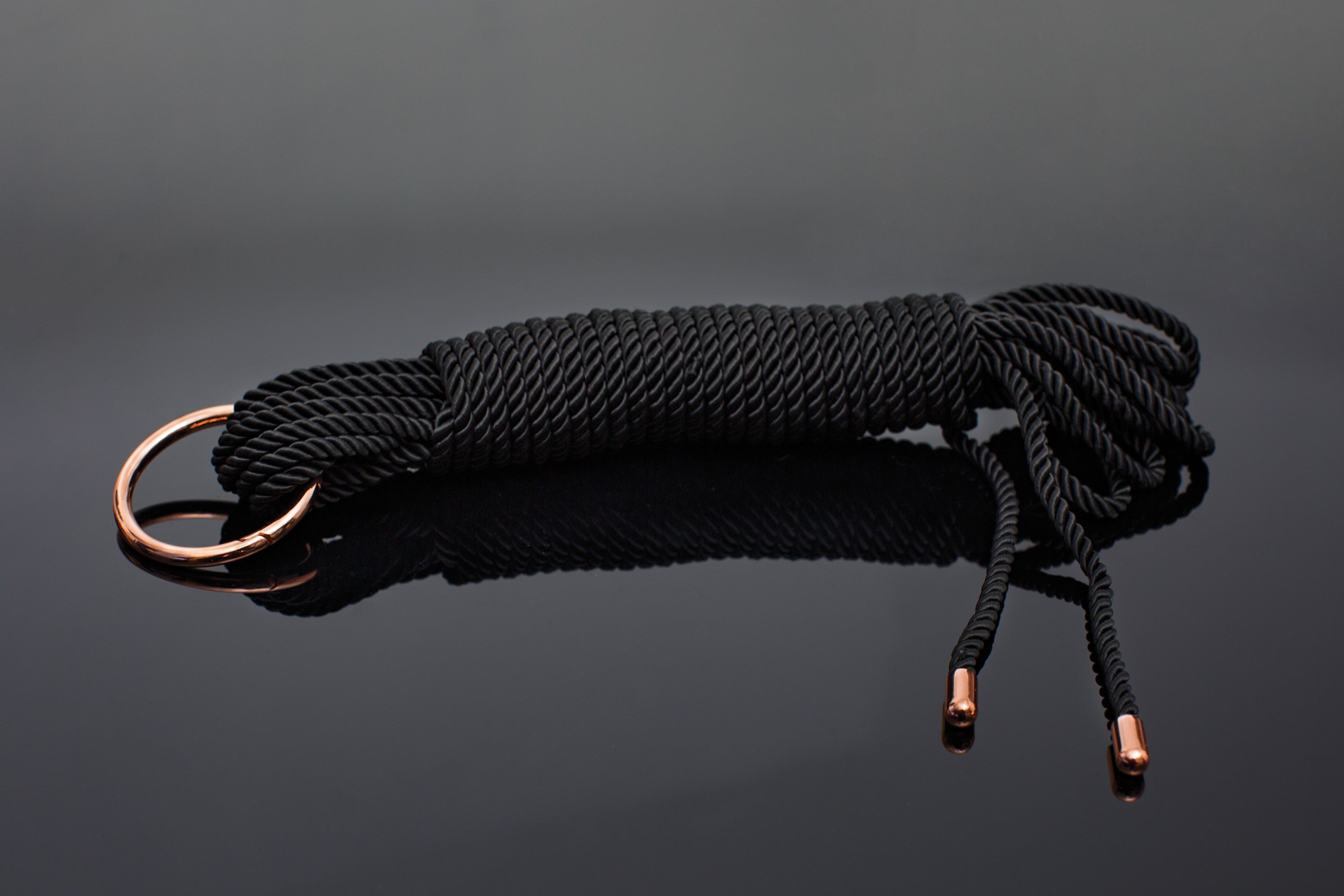 close up of silky black bedroom rope with rose gold metal tipped ends and a large carabiner o-ring.