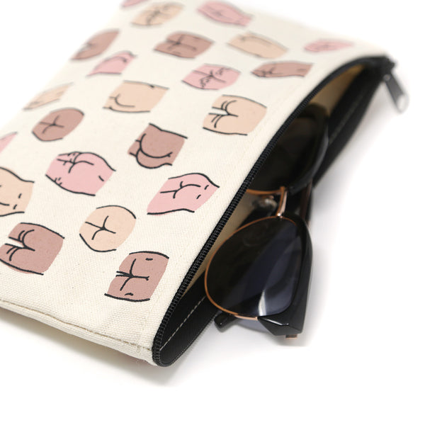a close up of the open zipper with sunglasses coming out. The pouch is a nuetral colored canvas pouch with several skin tones of butt drawings on it