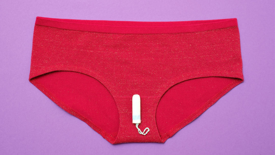 Tampon resting on red underpants against a purple background