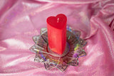 red heart shaped wax play pillar candle on lotus dish ontop of pink cloth