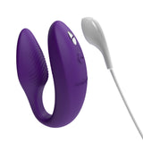 hands-free wearable c-shaped purple We-Vibe sync with the charging cord close to the magnetic port. meant to show that the toy is rechargeable