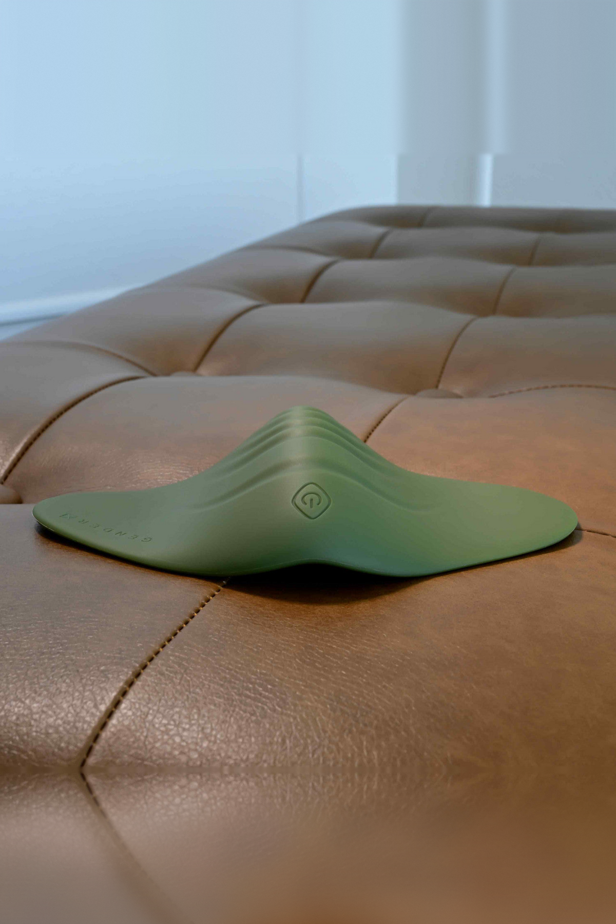 All the Pleasure grinding pad in Olive Green lying flat on a brown leather ottoman, showing its low ridged profile and button
