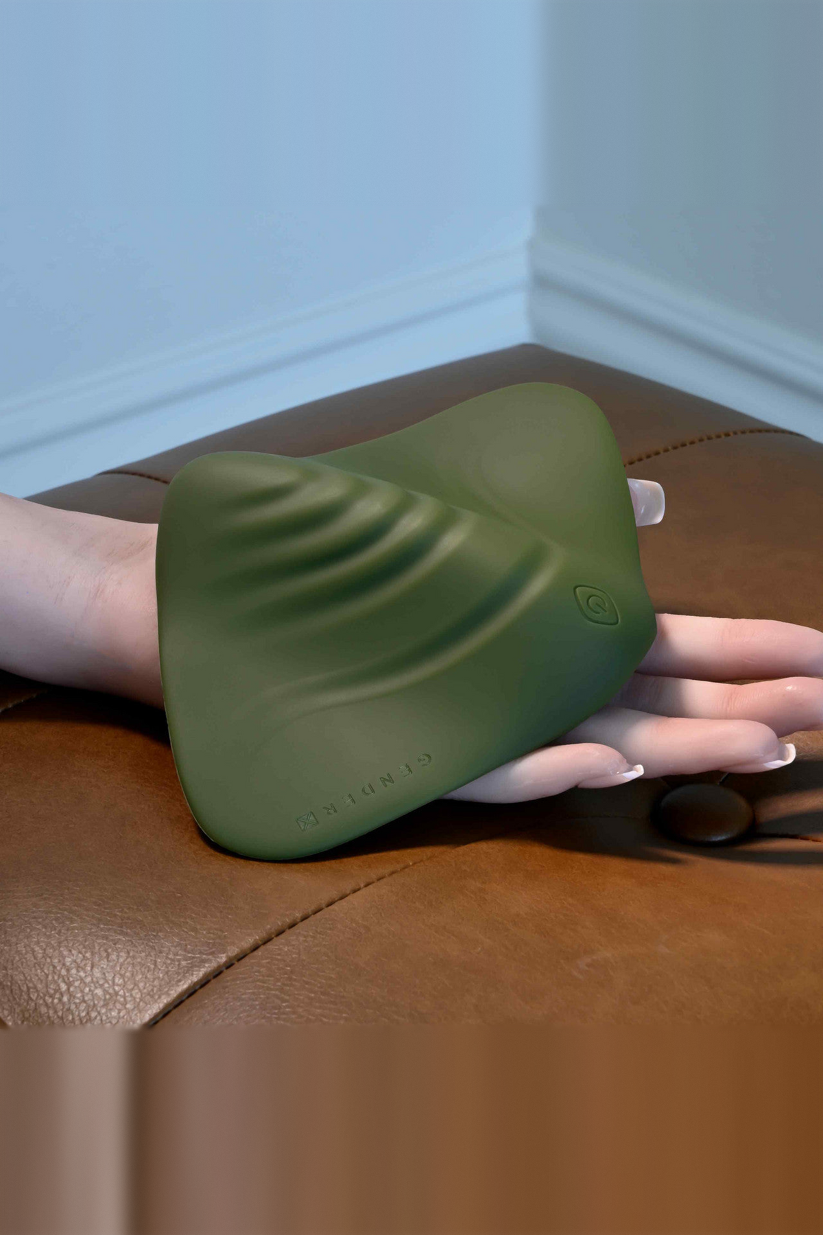 Hand resting beside the All the Pleasure grinding pad in Olive Green on a leather ottoman, showing its size and curved ridges