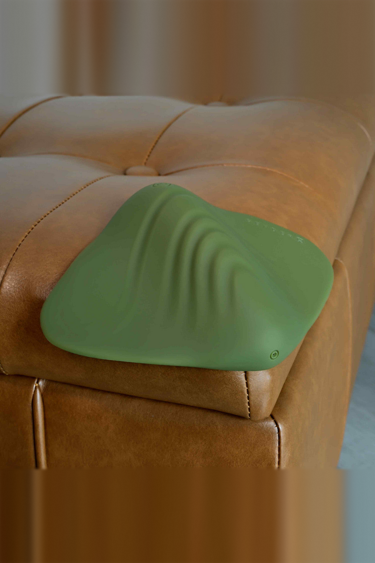 All the Pleasure vibrating grinding pad in Olive Green on the corner of a leather ottoman, showing its wavy textured surface