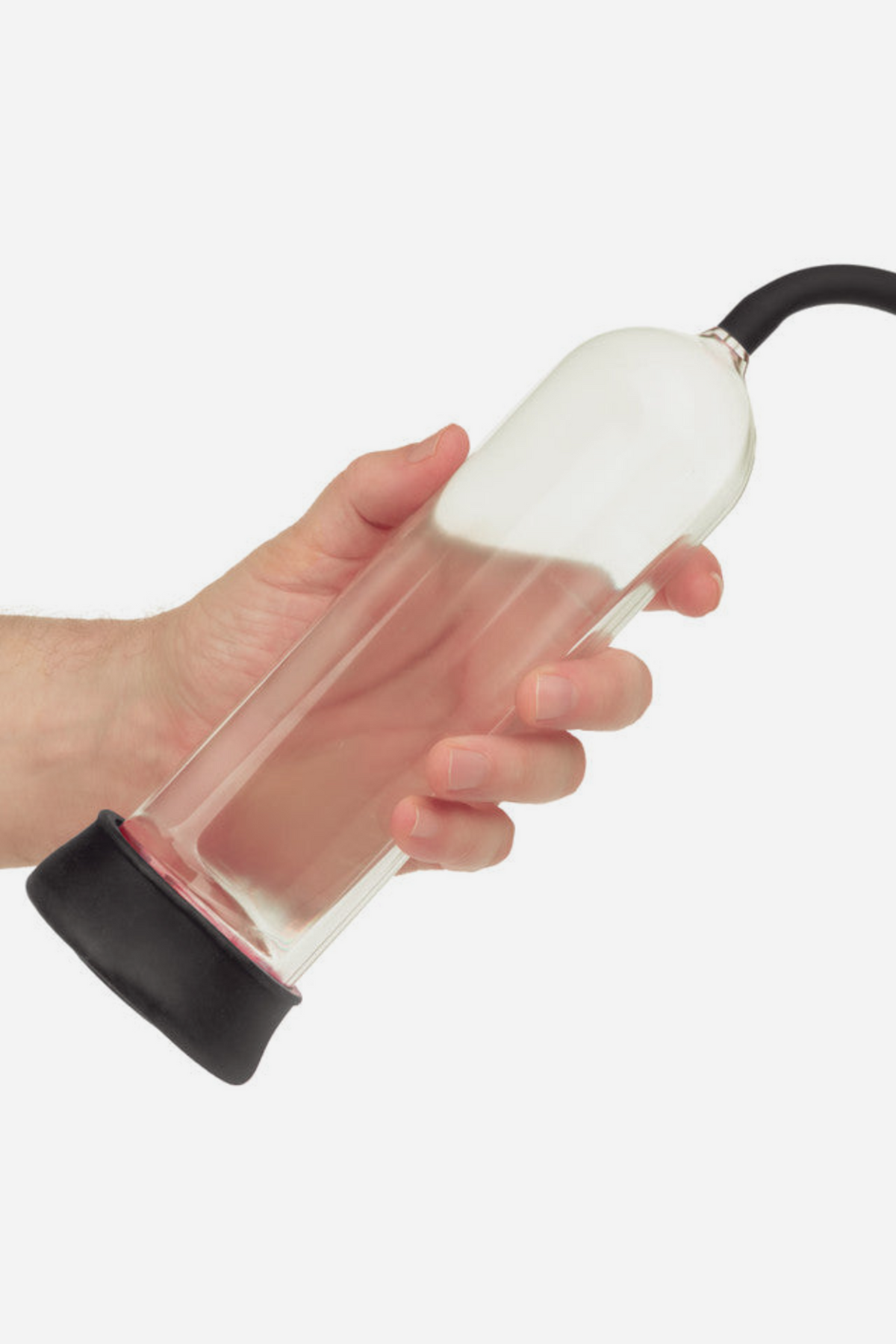 Hand holding the clear At Your Peak penis pump cylinder with its black sleeve and air hose, showing its size and measurement markings, on grey