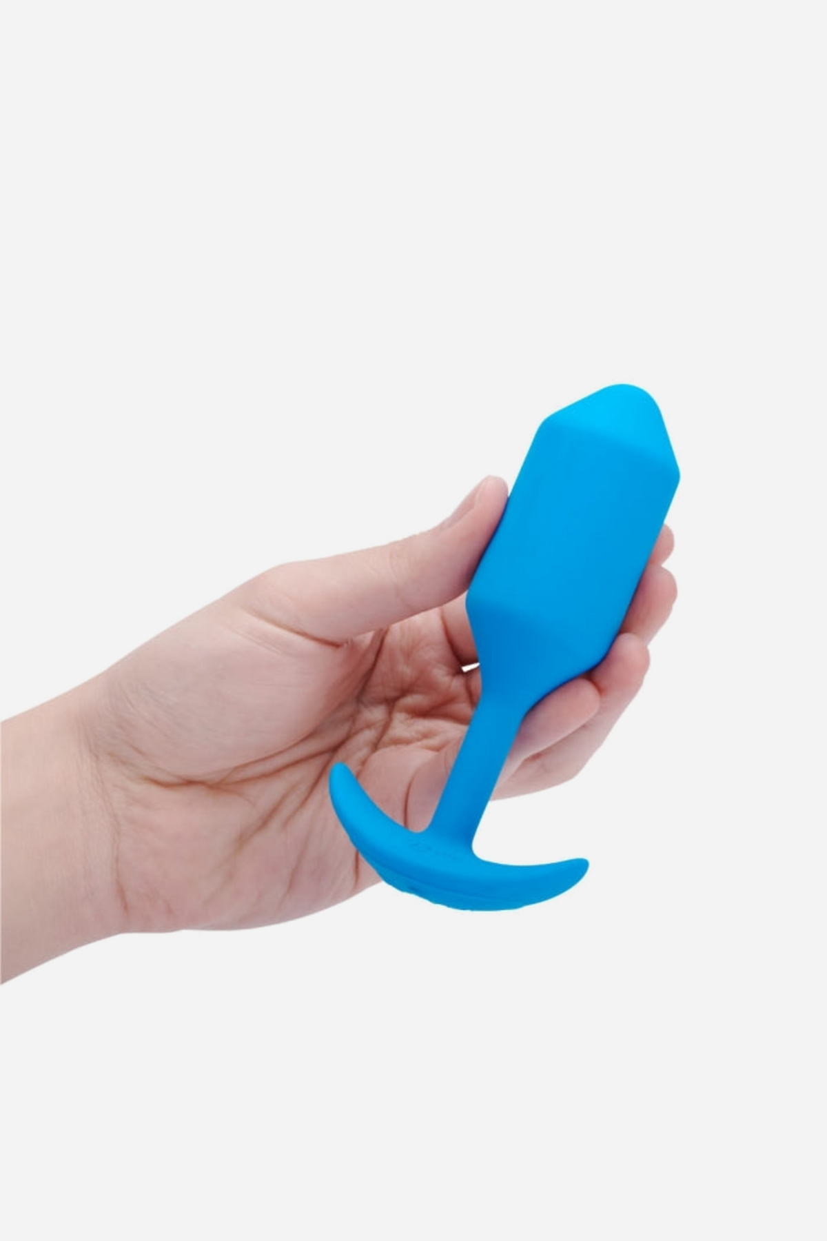 A hand holding the blue B-Vibe Vibrating Snug Plug 3 Large on grey, showing how the weighted bulb fills the palm above the flared T-shaped base.