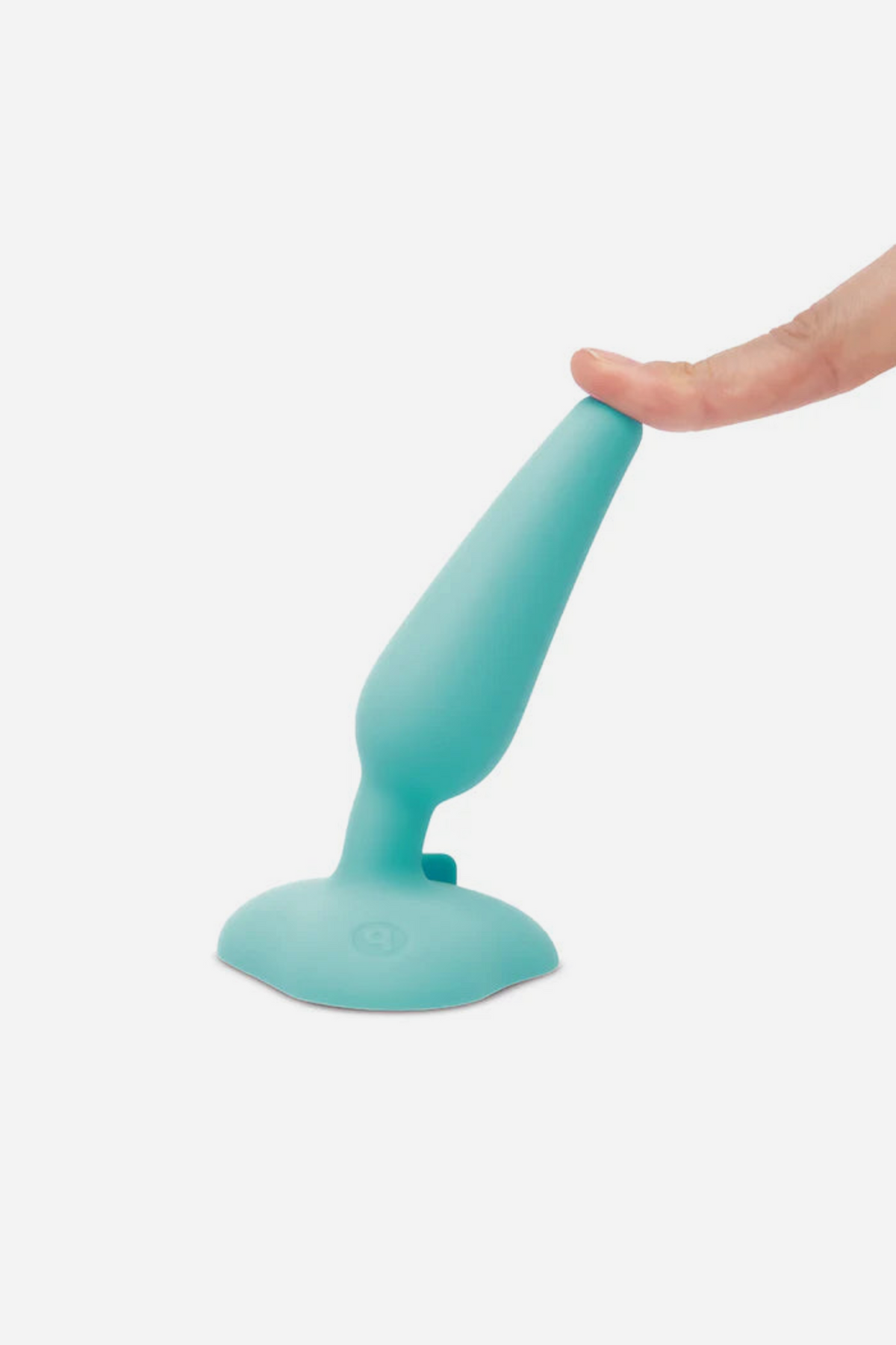 Finger pressing the tip of the teal B-Vibe plug so it bends on its suction base, showing the soft, flexible body-safe silicone