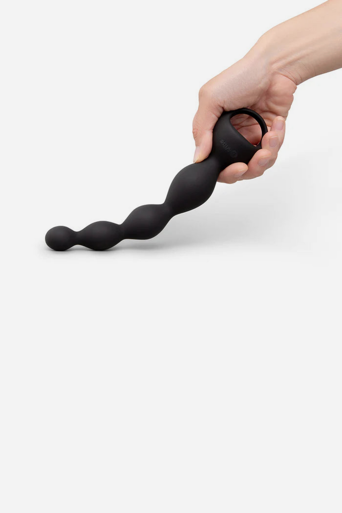 Hand flexing the black B-Vibe Earth Rumbling vibrating anal beads by the ring handle to show the bendable silicone bead shaft, on grey