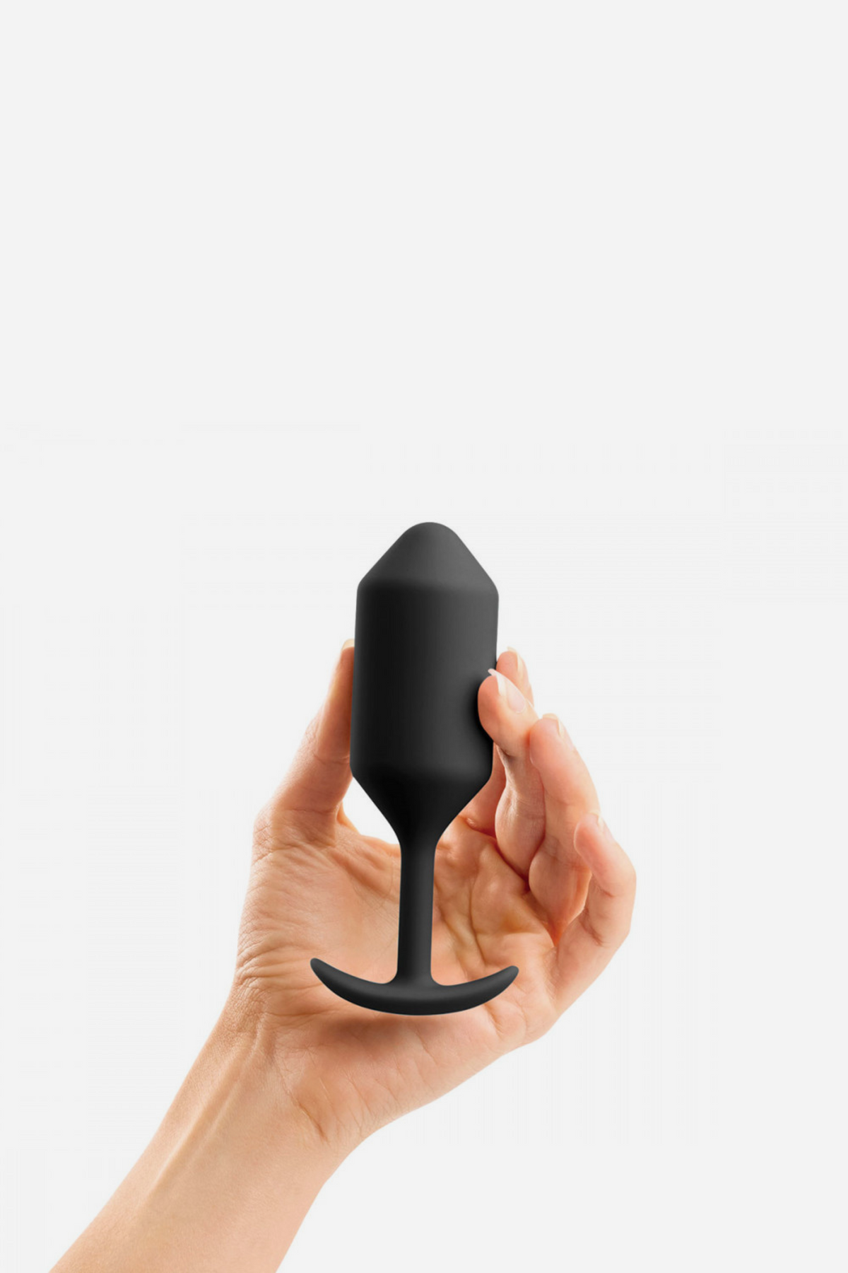 Hand holding the B-Vibe Snug Plug 3 weighted butt plug in Black, showing its size, weighted bulb and flared T-base on grey