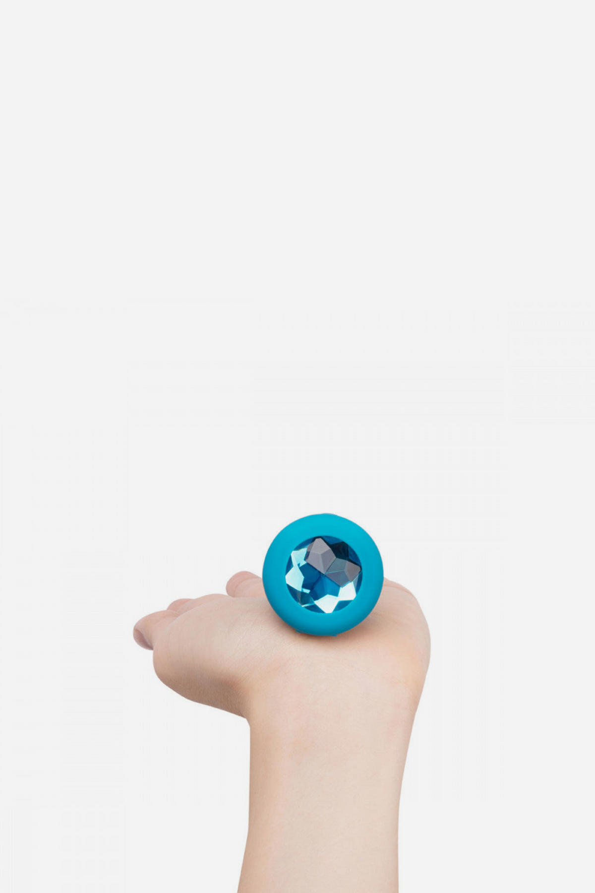 Hand holding the aqua B-Vibe Vibrating Jewel Plug, showing its small to medium size and the shimmering blue jewel on the flared base
