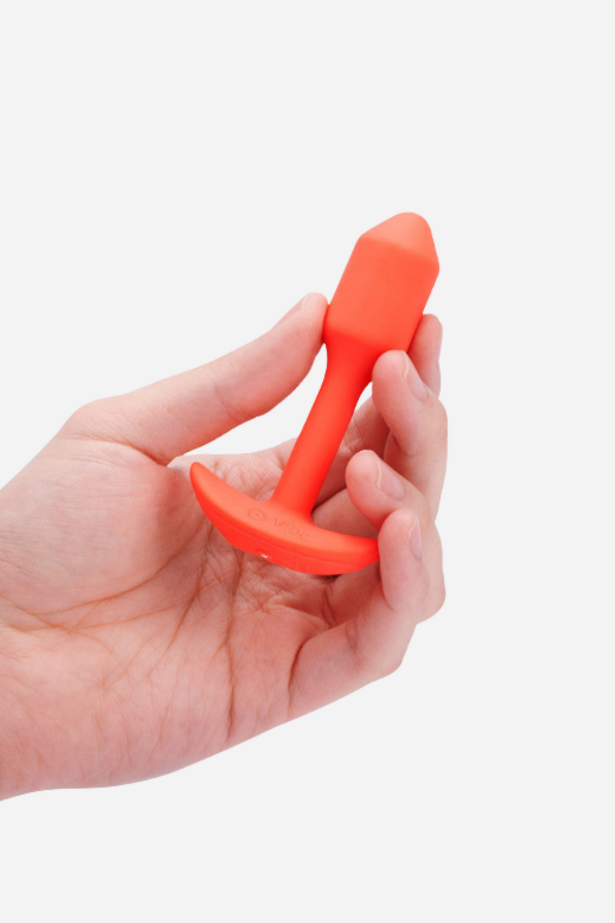 Hand holding the orange B-Vibe Vibrating Snug Plug 1 small between the fingers to show its compact beginner size, on grey